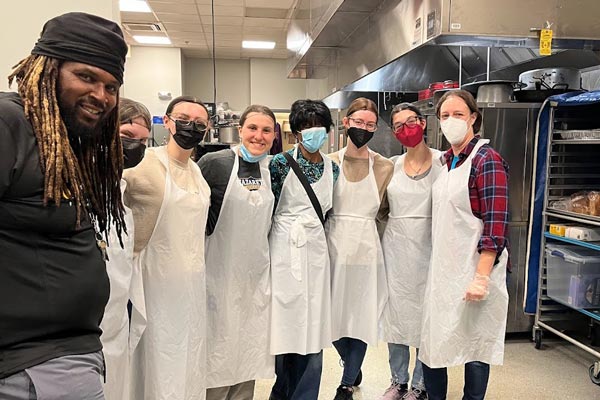 Students and staff in white aprons and masks in the kitchen at Central Union Mission, Washington, DC