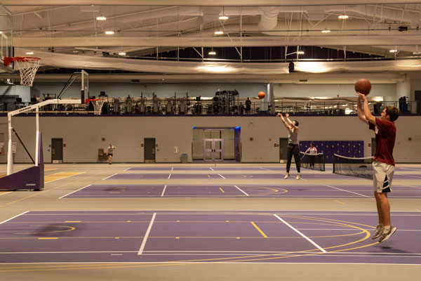 Students shooting hoops on basketball courts inside an indoor track